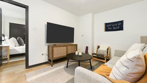 A modern living room with a flat-screen TV, a wooden cabinet, a round coffee table, and a sofa. - ★ HostWise Stays ★ Pet Friendly, Butler St. Apt with Private Entrance (Pittsburgh)