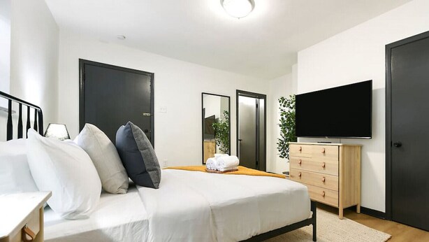 A modern bedroom with a bed, bedside tables, a dresser, a TV, and a mirror. - ★ HostWise Stays ★ Pet Friendly, Butler St. Apt with Private Entrance (Pittsburgh)