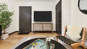 Una sala de estar moderna con un televisor de pantalla plana, un mueble de madera, una planta en maceta y un sillón acolchado.