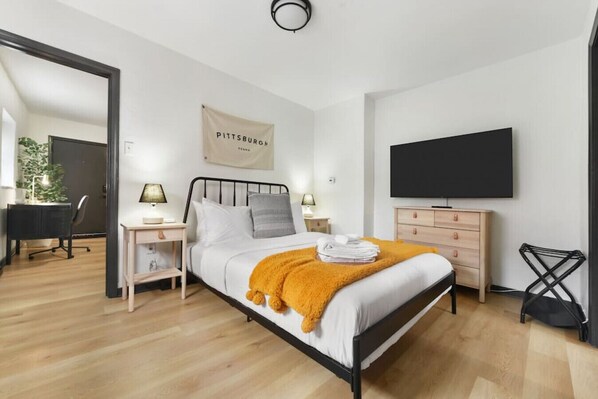 A modern bedroom with a bed, bedside tables, a TV, and a desk with a chair. - Butler St Cozy Retreat, Walk to Breweries & Shops (Pittsburgh)