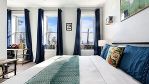 A hotel room with a large bed, a desk with books, and a window with curtains. - ★ HostWise Stays ★ Family Friendly, Great Area, Artist Abode! (Pittsburgh)