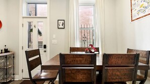 A dining area with a wooden table and benches, a window with curtains, and a wall-mounted map. - ★ HostWise Stays ★ Family Friendly, Great Area, Artist Abode! (Pittsburgh)