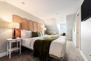 Une chambre moderne avec un grand lit, une table de chevet avec une lampe, une tête de lit en osier et une grande fenêtre.