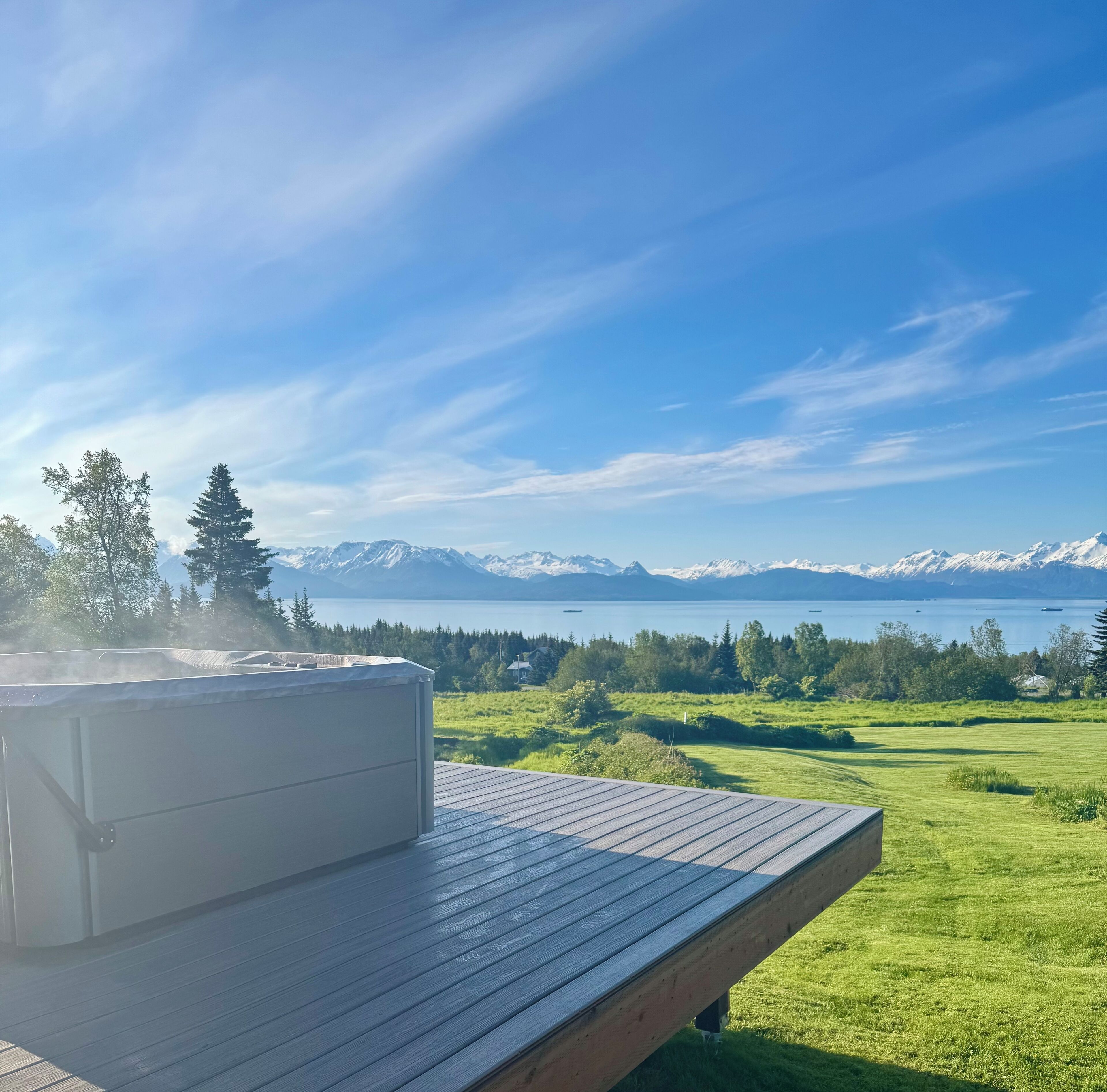 A hot tub on a wooden deck overlooking a lake with mountains in the distance.