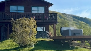 Eine zweistöckige Holzhütte mit einem Balkon, umgeben von einer Wiese und einem Berg im Hintergrund.