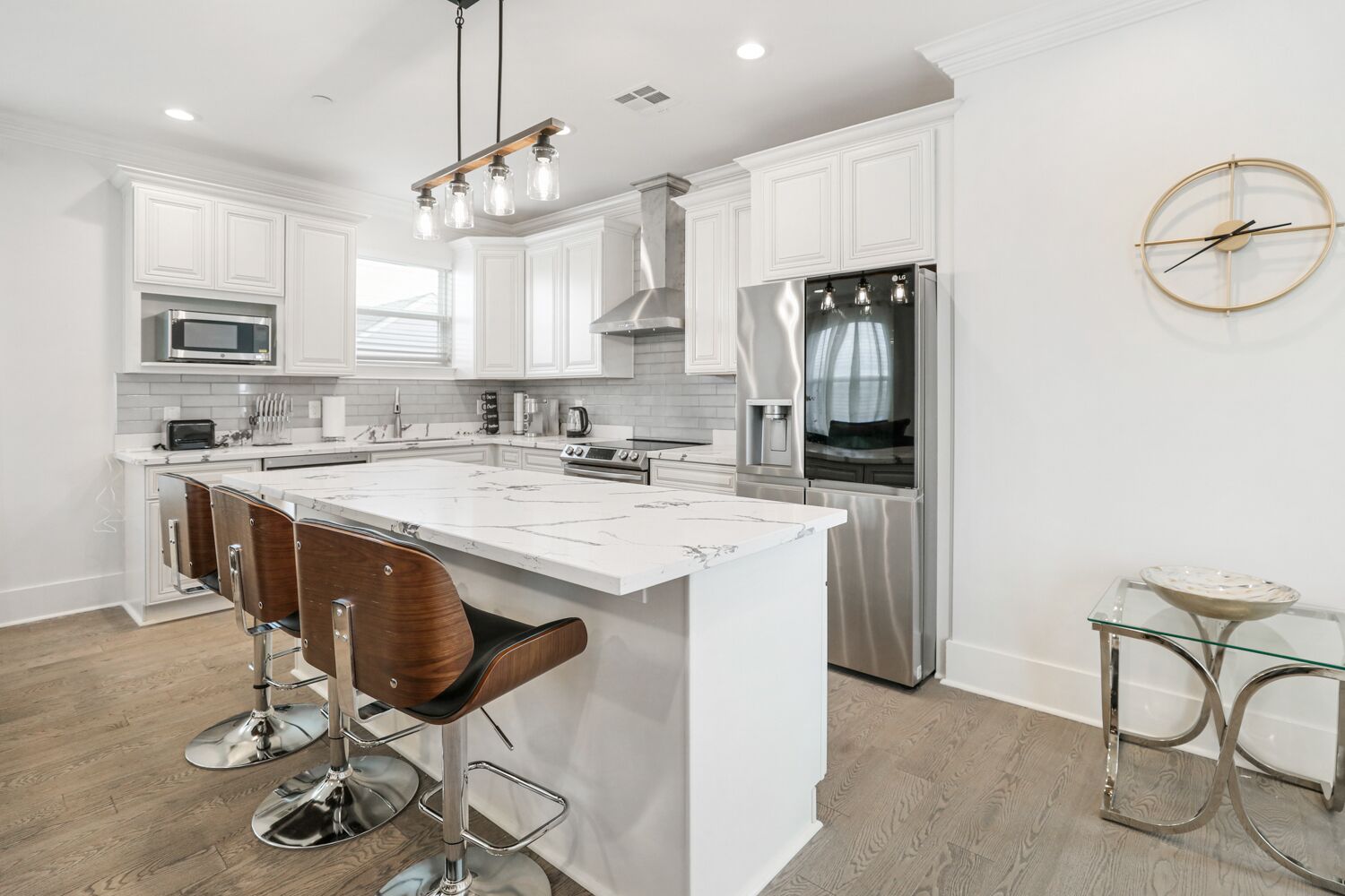 A modern kitchen with white cabinetry, stainless steel appliances, and a central island with bar stools.