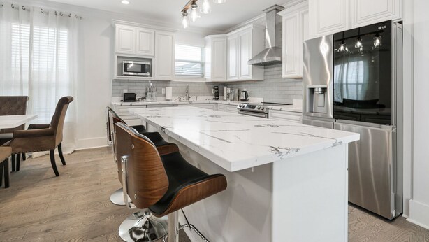 A modern kitchen with white cabinetry, a large island, stainless steel appliances, and a dining area with bar stools. - New Constructed Luxury 3-BD House in Mid-City (New Orleans)