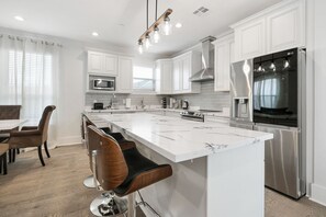 Una cocina moderna con armarios blancos, una isla grande, electrodomésticos de acero inoxidable y un comedor con taburetes de bar.