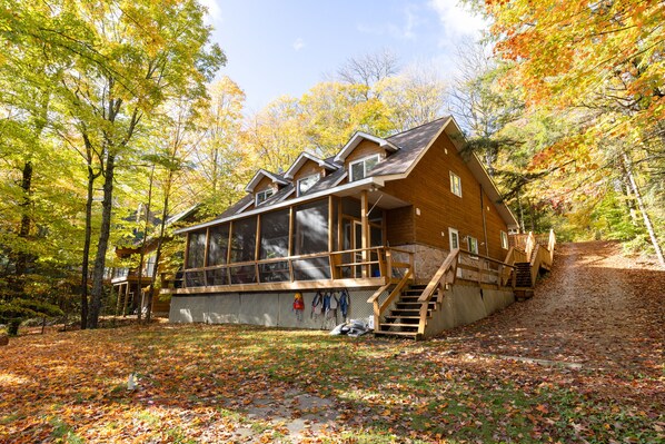 A cabin with a large deck, a covered porch, and a staircase leading to a second level. - Modern cottage escape in Muskoka (Huntsville)