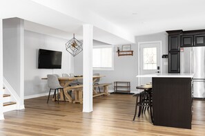 A modern kitchen with dark cabinets, a stainless steel refrigerator, and a wooden dining area with a TV mounted on the wall. - Modern cottage escape in Muskoka (Huntsville)