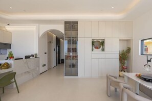 A modern kitchen with white cabinetry, a marble countertop, and a dining area with a table and chairs.