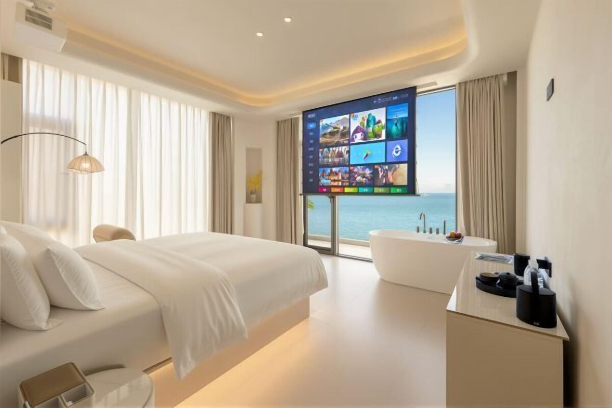 Habitación de hotel moderna con una cama grande, una bañera, un escritorio y un televisor que muestra varios canales.