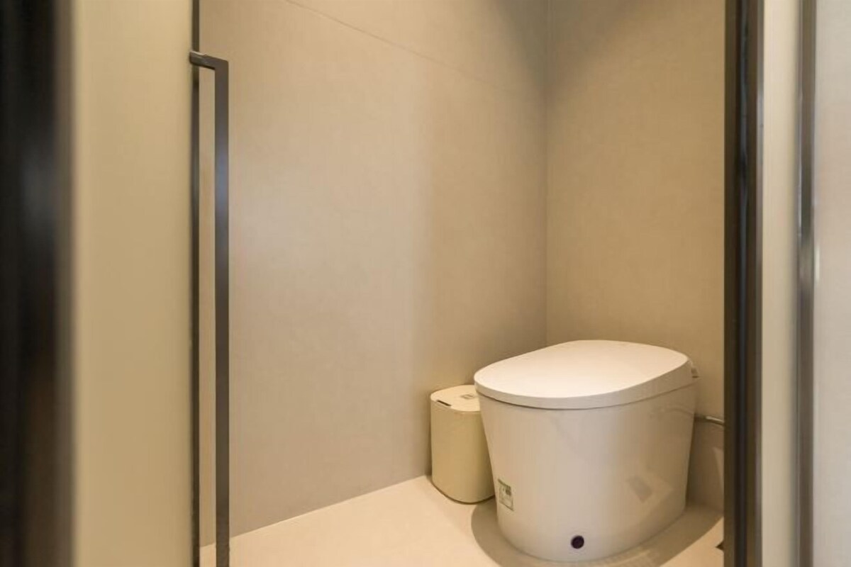 Un baño pequeño y cerrado con inodoro, un bote de basura y zona de ducha.