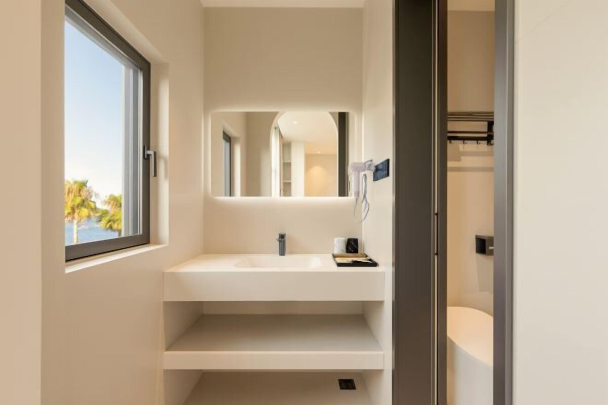 Un baño moderno con un amplio ventanal, un lavamanos blanco y un espejo.