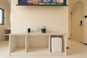 Una habitación de hotel con una mesa consola blanca, un televisor de pantalla plana montado encima y un refrigerador pequeño blanco.