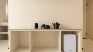 A minimalist kitchenette with a white countertop, a coffee maker, a kettle, and a small appliance.