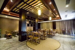 Une salle à manger d’hôtel avec de nombreuses tables et chaises, un pilier central et un plafond doté d’un éclairage encastré.