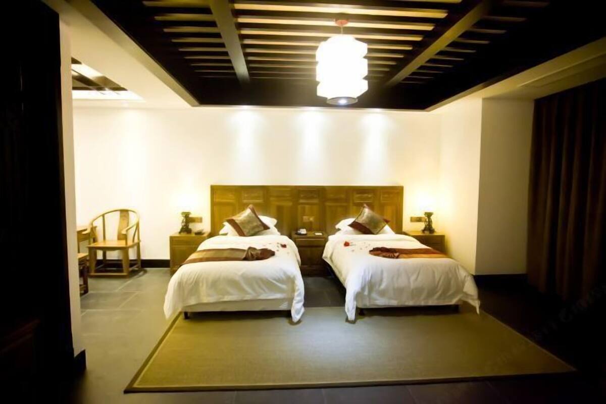 Ein Hotelzimmer mit zwei Betten, einem Holzkopfende, Nachttischlampen, einem Sessel und einem großen Fenster.