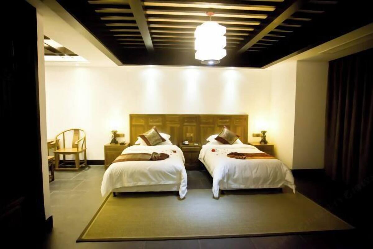 Ein Hotelzimmer mit zwei Betten, einem Holz-Kopfteil, Nachttischen, einem Sessel und einer großen Leuchte.