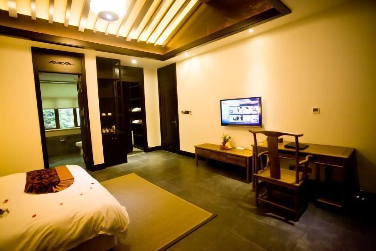 Ein Hotelzimmer mit Bett, Schreibtisch, Fernseher und einem durchgegangenen Tür sichtbaren Badezimmer.