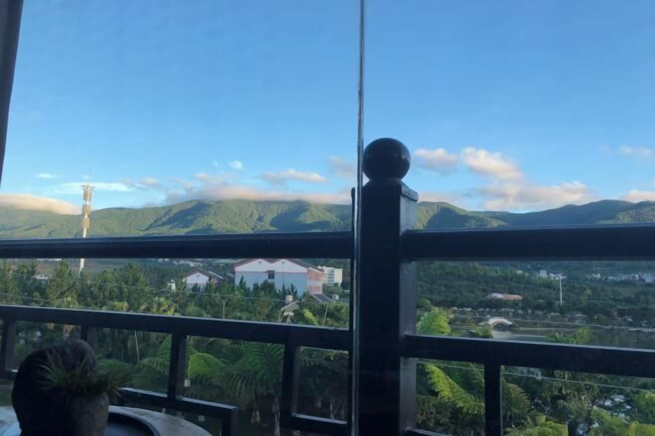 Un balcón con vistas a un paisaje montañoso, una torre distante y algunos edificios.