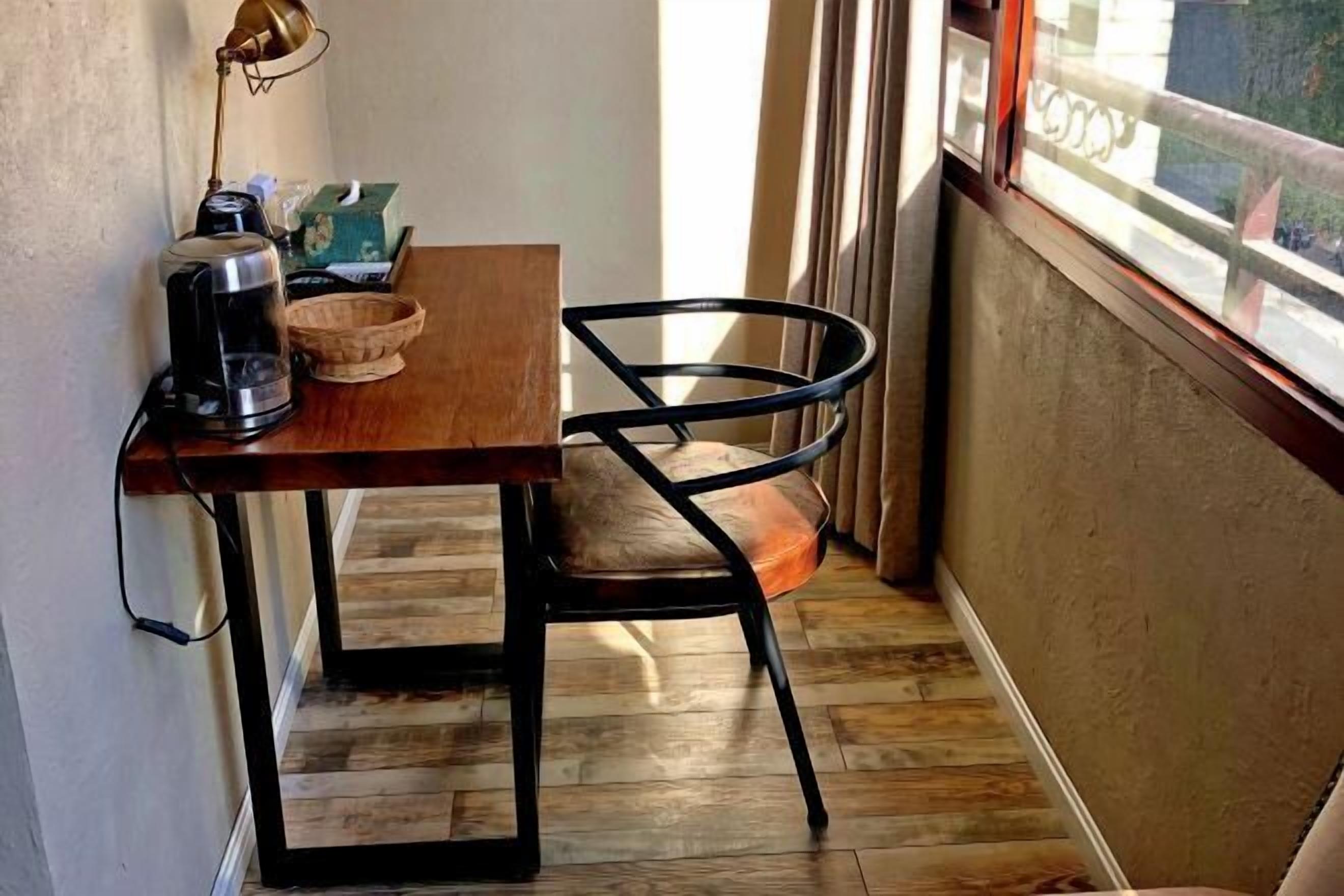Una pequeña mesa de madera con una silla negra, una cafetera y un bol.