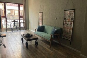 A room with a green sofa, a small table, a hanging tapestry, and a view of a balcony.