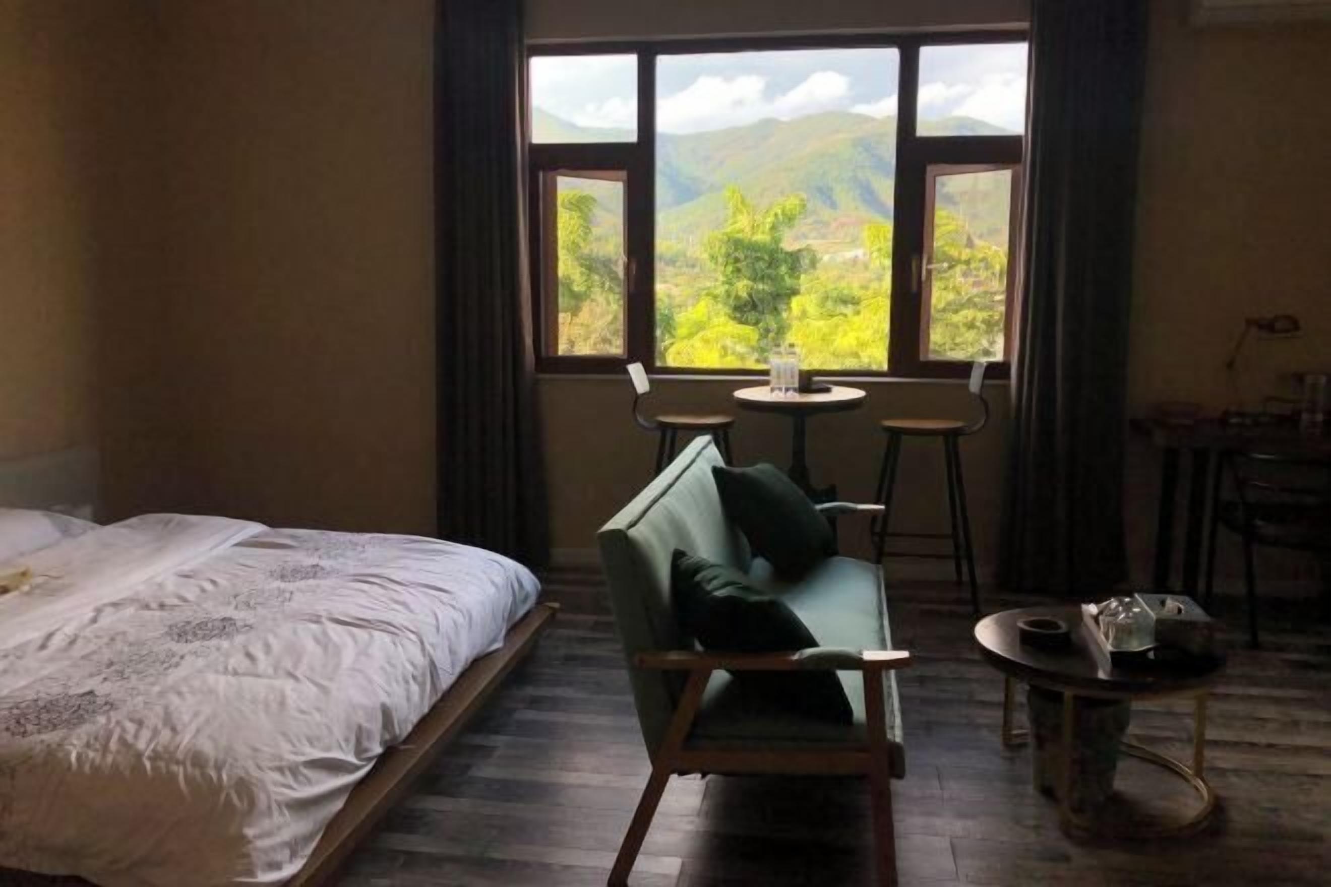 Una habitación con una cama, un sofá verde, una mesita y una ventana con vistas a montañas.