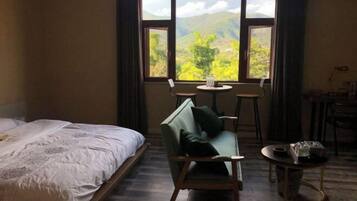 Una habitación con una cama, un sofá verde, una mesita y una ventana con vistas a montañas.