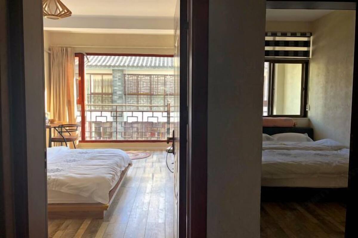 A room with two beds, a wooden floor, a balcony with a view, and a traditional-style window.