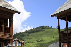 Una cabaña de madera con balcón, rodeada por una ladera cubierta de hierba y un cielo despejado.