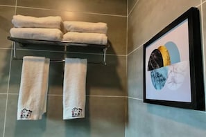 Um banheiro com um porta-toalhas com vários toalhas brancas, uma obra de arte emoldurada na parede e um chão em mosaico.