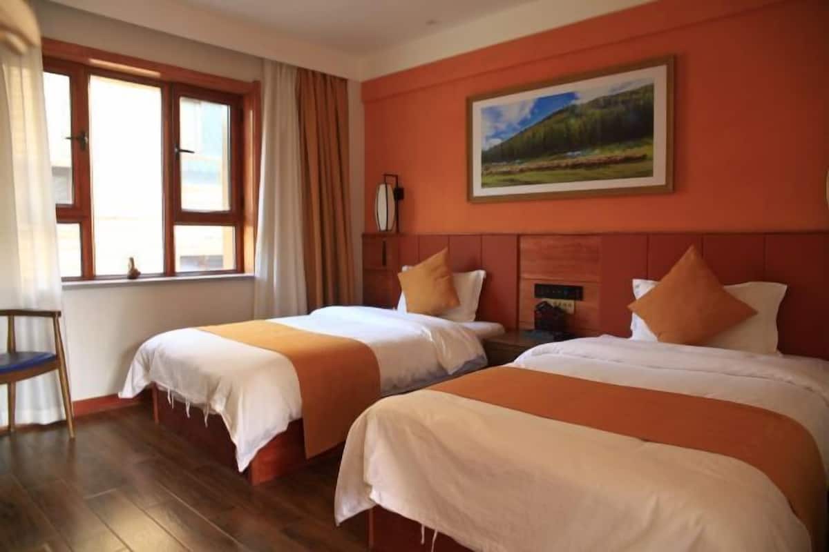 Habitación de hotel con dos camas, una ventana con cortinas, un cuadro en la pared y suelo de madera.