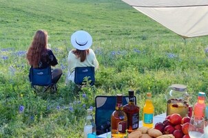 Dos personas sentadas en sillas en un campo de césped, con una mesa de comida y bebidas frente a ellas.