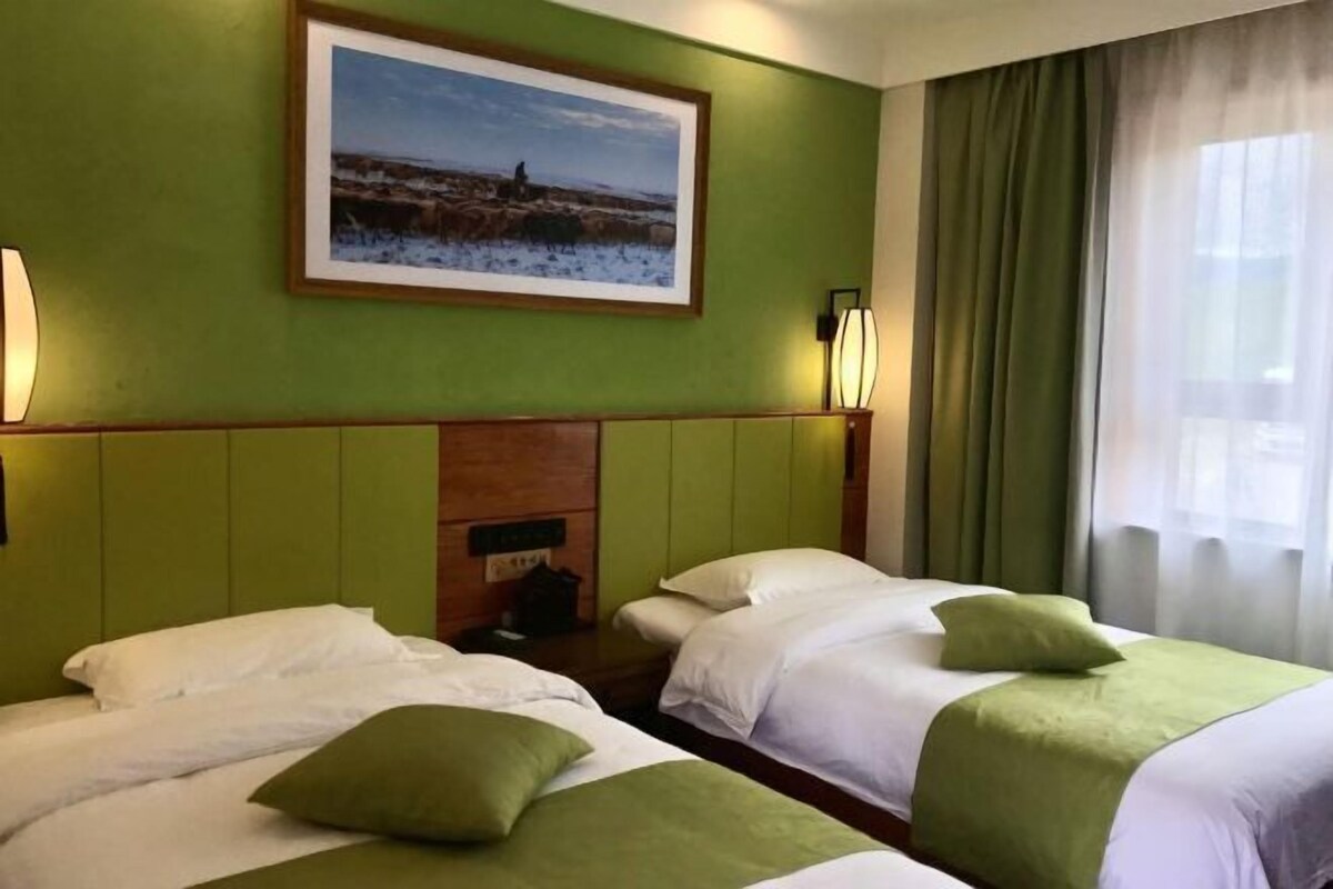 A hotel room with two beds, a green wall, a framed picture, and a window with curtains.