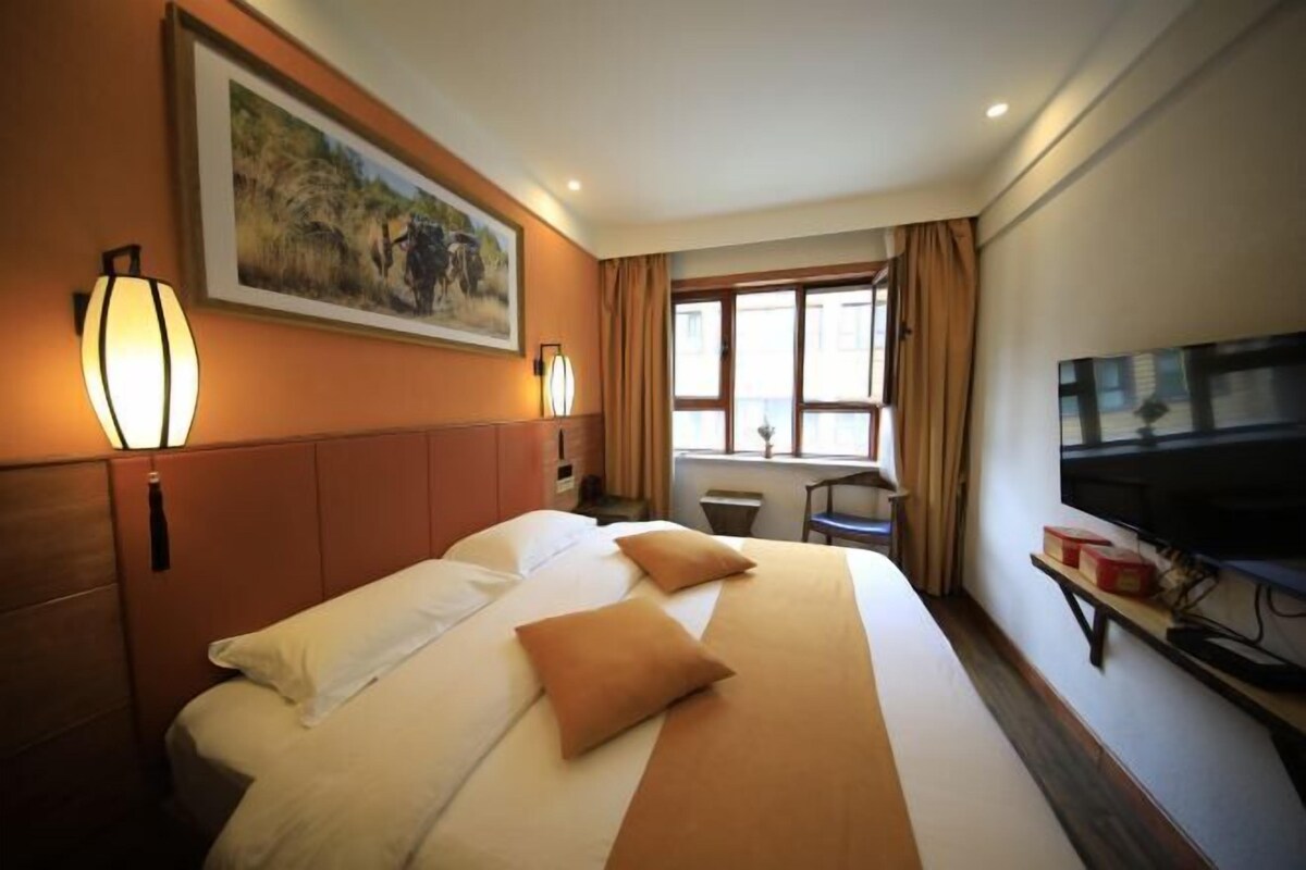 A hotel room with a large bed, a television, a painting on the wall, and a window with curtains.