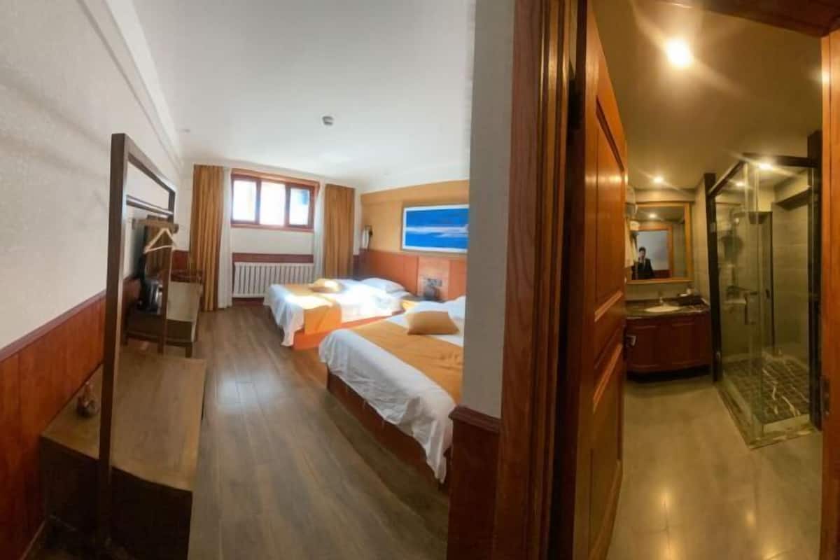 Habitación de hotel con dos camas, baño con ducha y vista al cielo a través de una ventana.