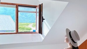 Habitació amb finestral a la llum del cel, vista a un paisatge verd i una persona portant un barret.