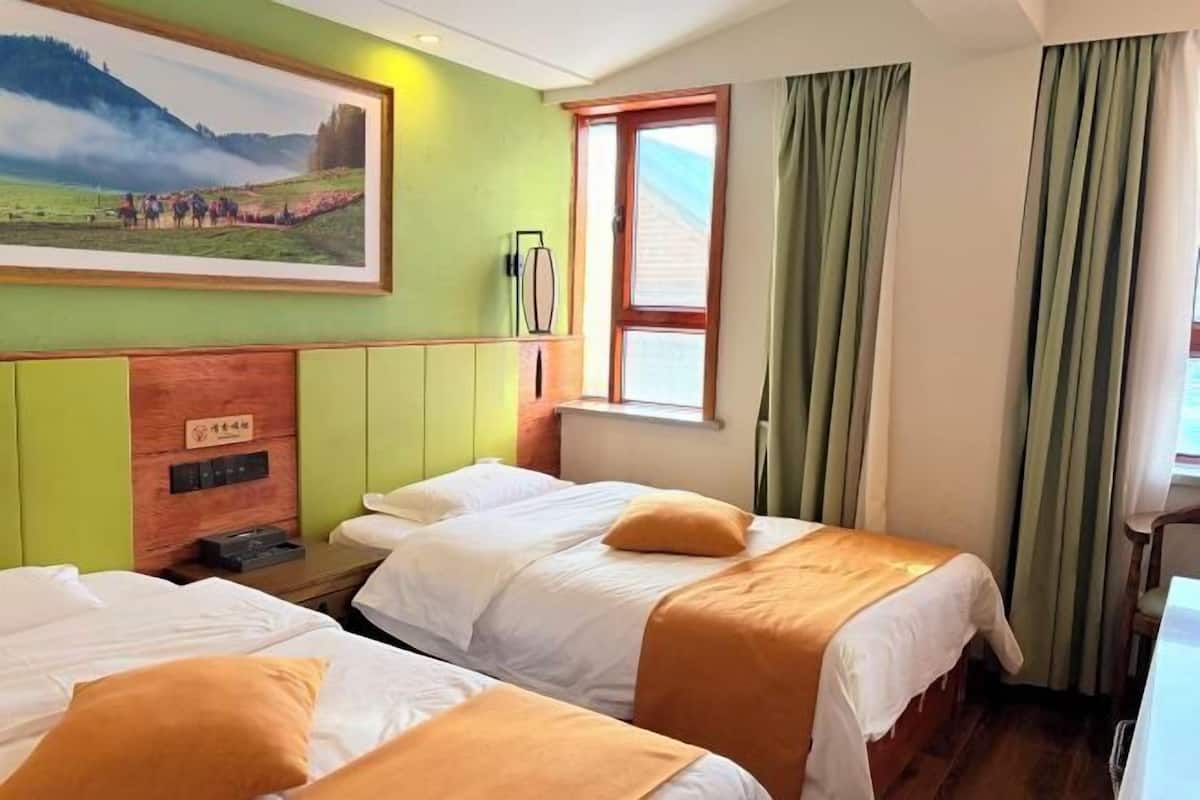 Habitación de hotel con dos camas, un cuadro en la pared, una ventana con cortinas y un cabecero de madera.