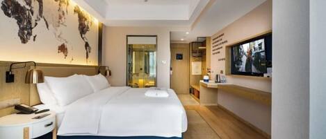 A hotel room with a large bed, a desk with a lamp, a world map on the wall, and a TV on the opposite wall.