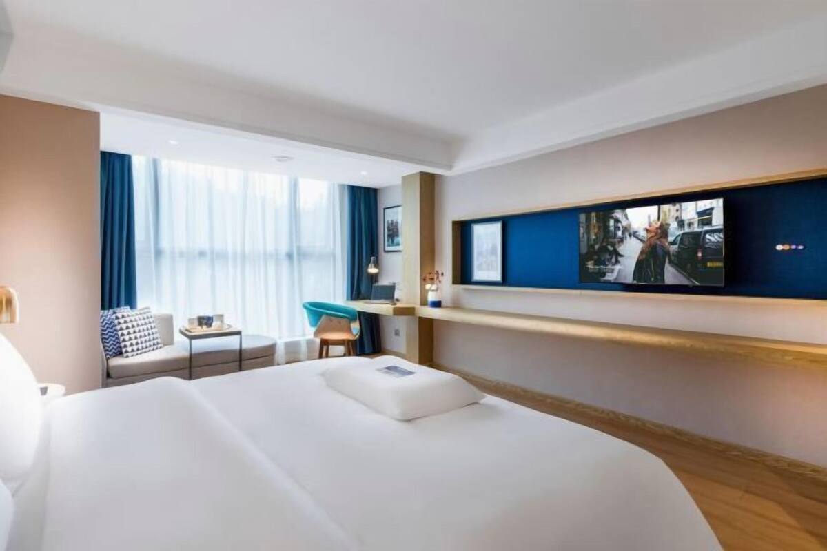 A hotel room with a large bed, a desk, a chair, and a television mounted on the wall.