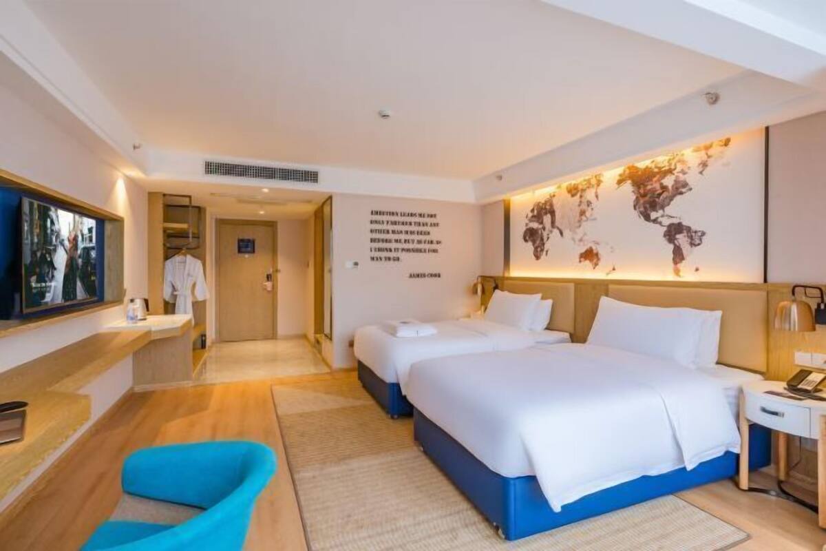 A hotel room with a large bed, a desk, a chair, and a world map on the wall.