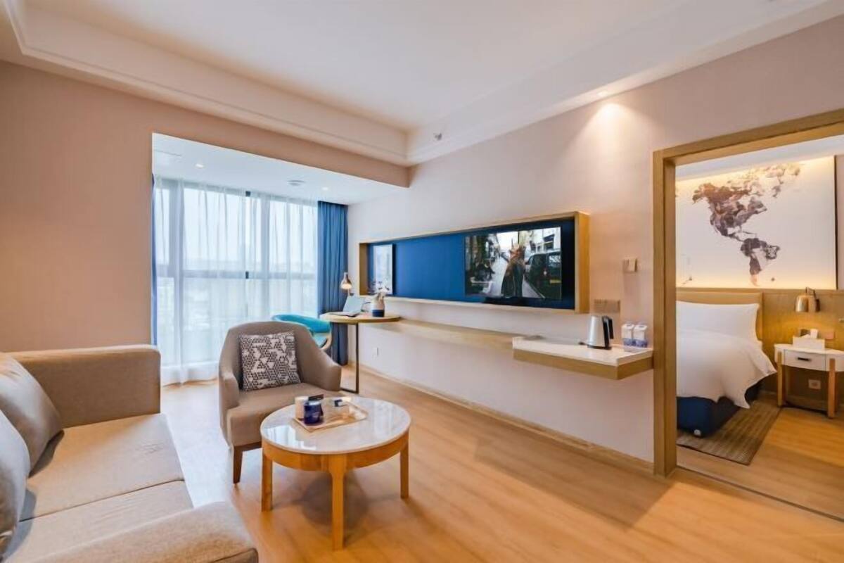 A modern hotel room with a sofa, a coffee table, a TV, a bed, and a world map artwork.