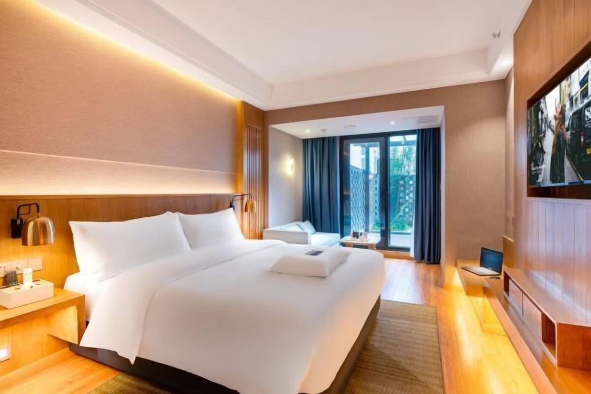 A hotel room with a large bed, a desk, a TV, and a window with curtains.