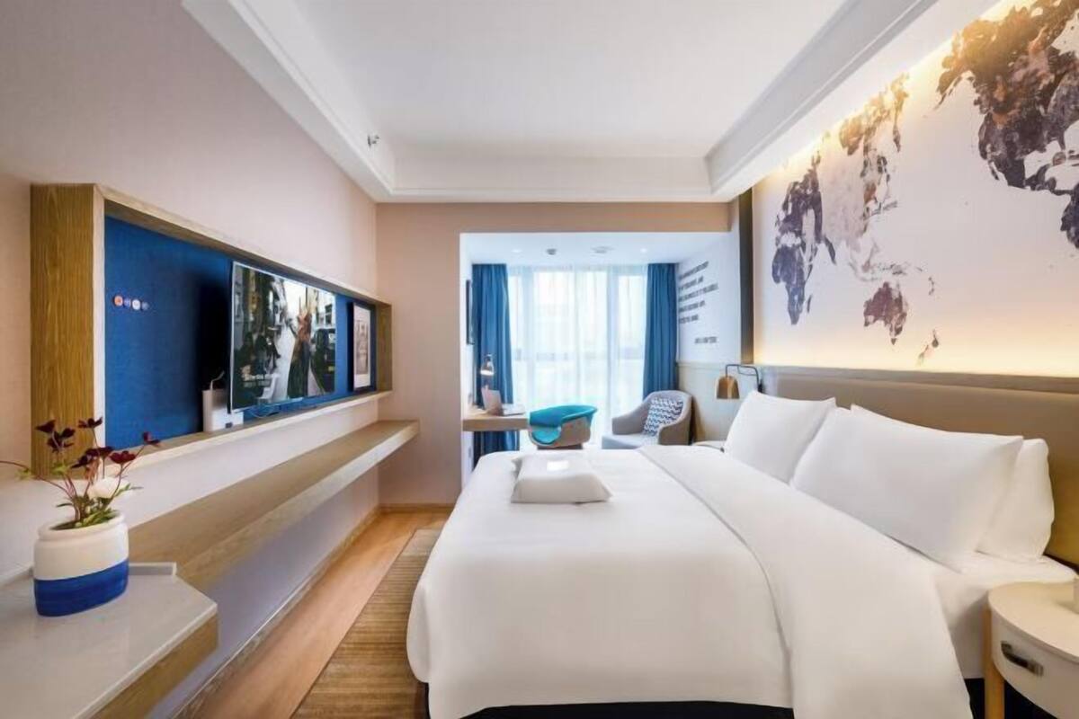 A hotel room with a large bed, a flat-screen TV, a desk with a chair, and a world map on the wall.