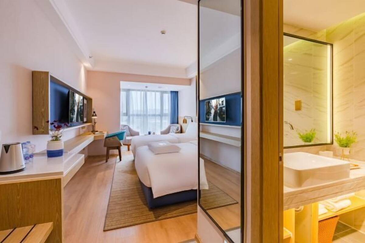 A modern hotel room with a bed, bedside table, TV, and a large mirror.
