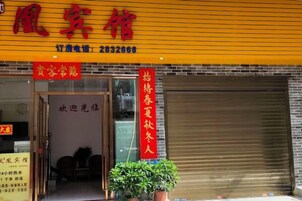 A hotel entrance with a red signboard, a closed shutter door, and a potted plant.