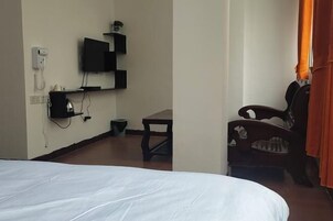 A hotel room with a bed, a desk, a chair, a television, and a telephone.