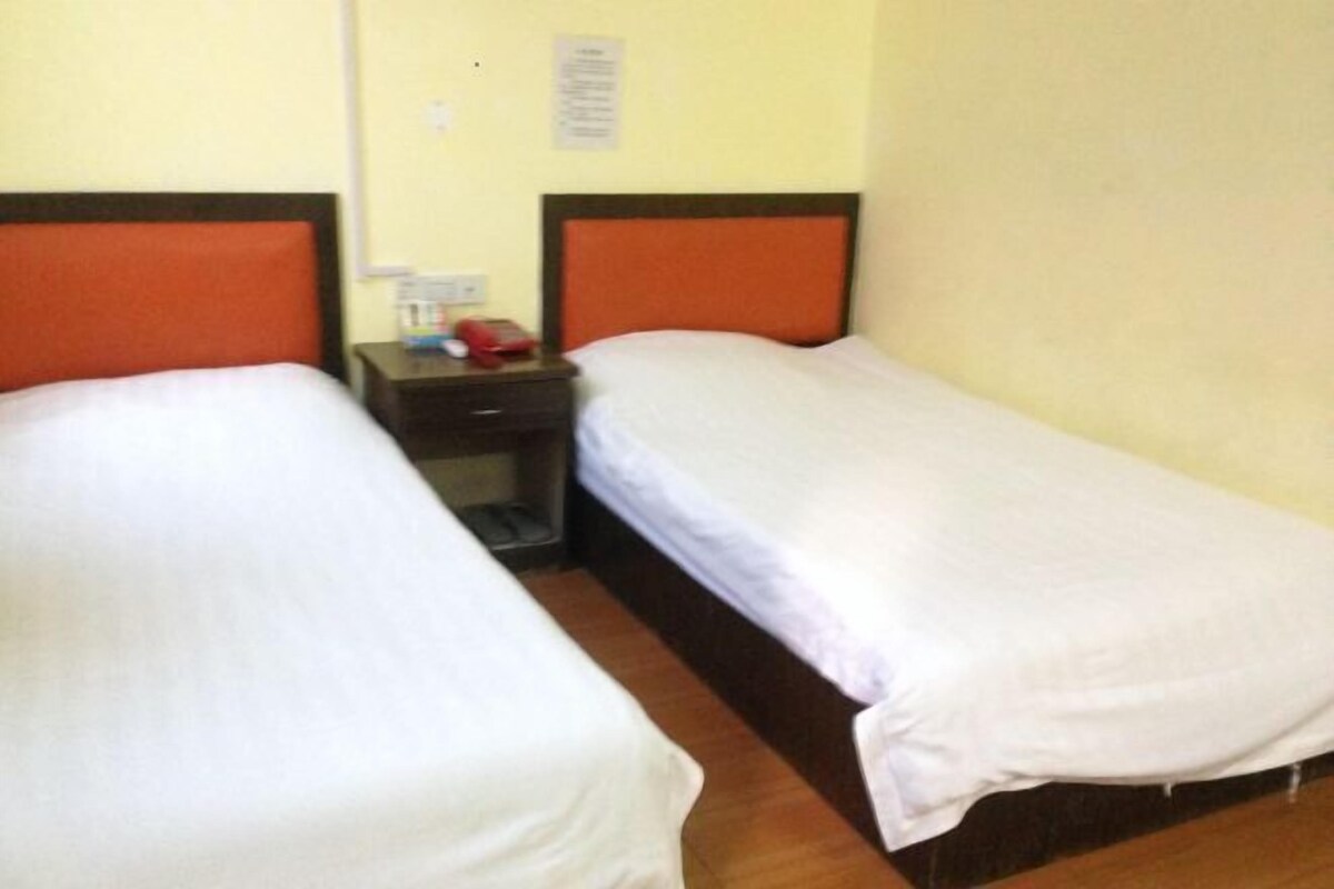A room with two single beds, each with a wooden headboard and a white mattress. There is a nightstand between the beds with a red object on it.