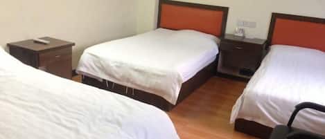 A hotel room with two single beds, wooden flooring, a small desk with a chair, and a nightstand with a remote control.